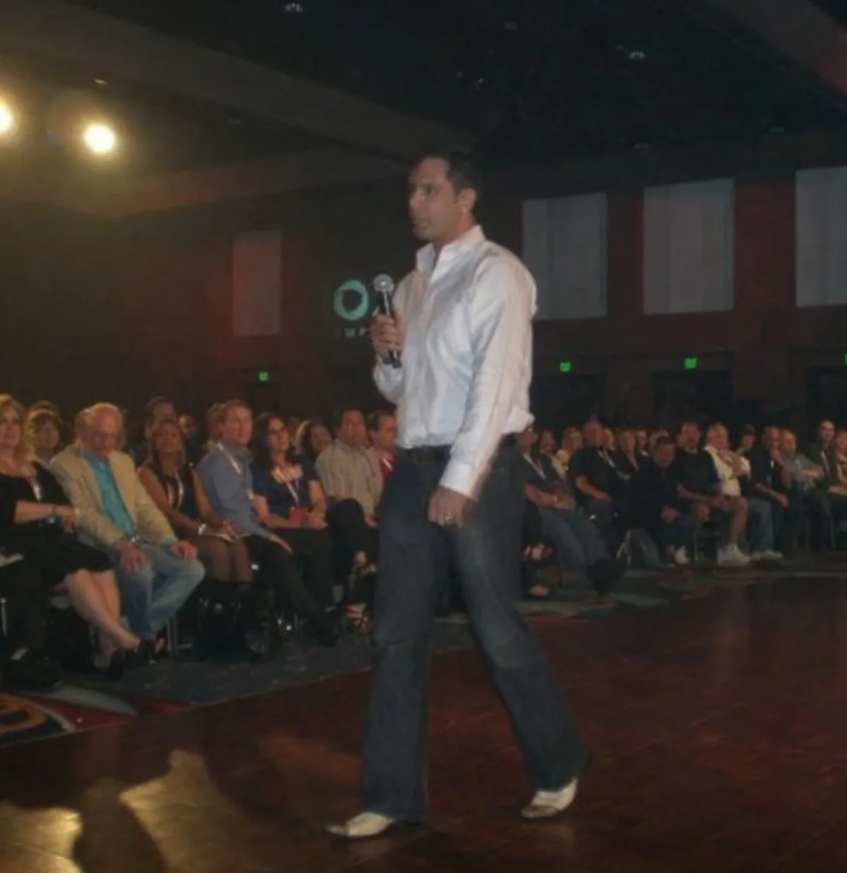 Shane James speaking with a microphone in front of a large seated audience