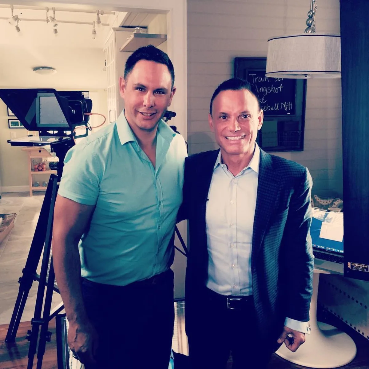 Shane James on a television set with a colleague, a teleprompter and camera rig behind them
